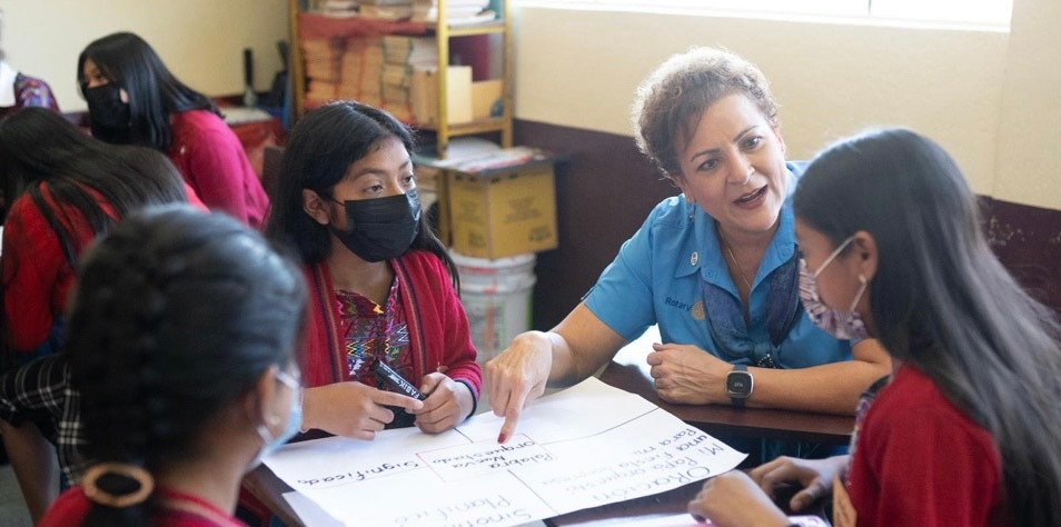 A teacher sites at a table with pupils looking at papers