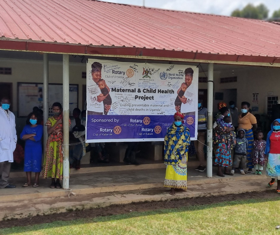 a group of people in masks standing in front of a Rotary banner in Uganda