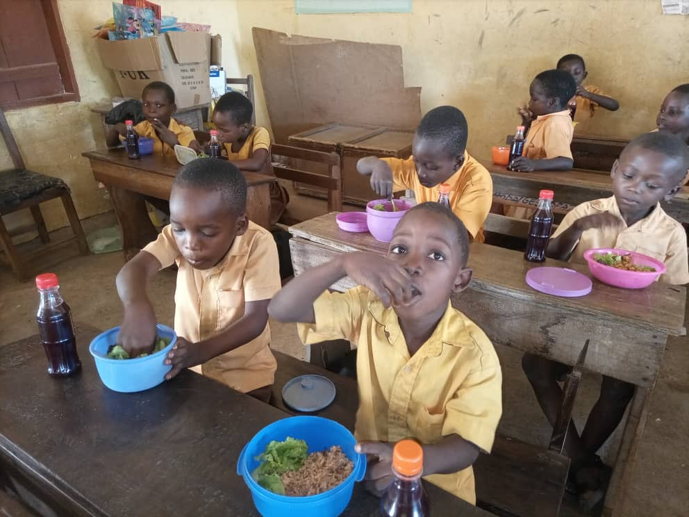 a group of children eating at a table in a classroom in Africa