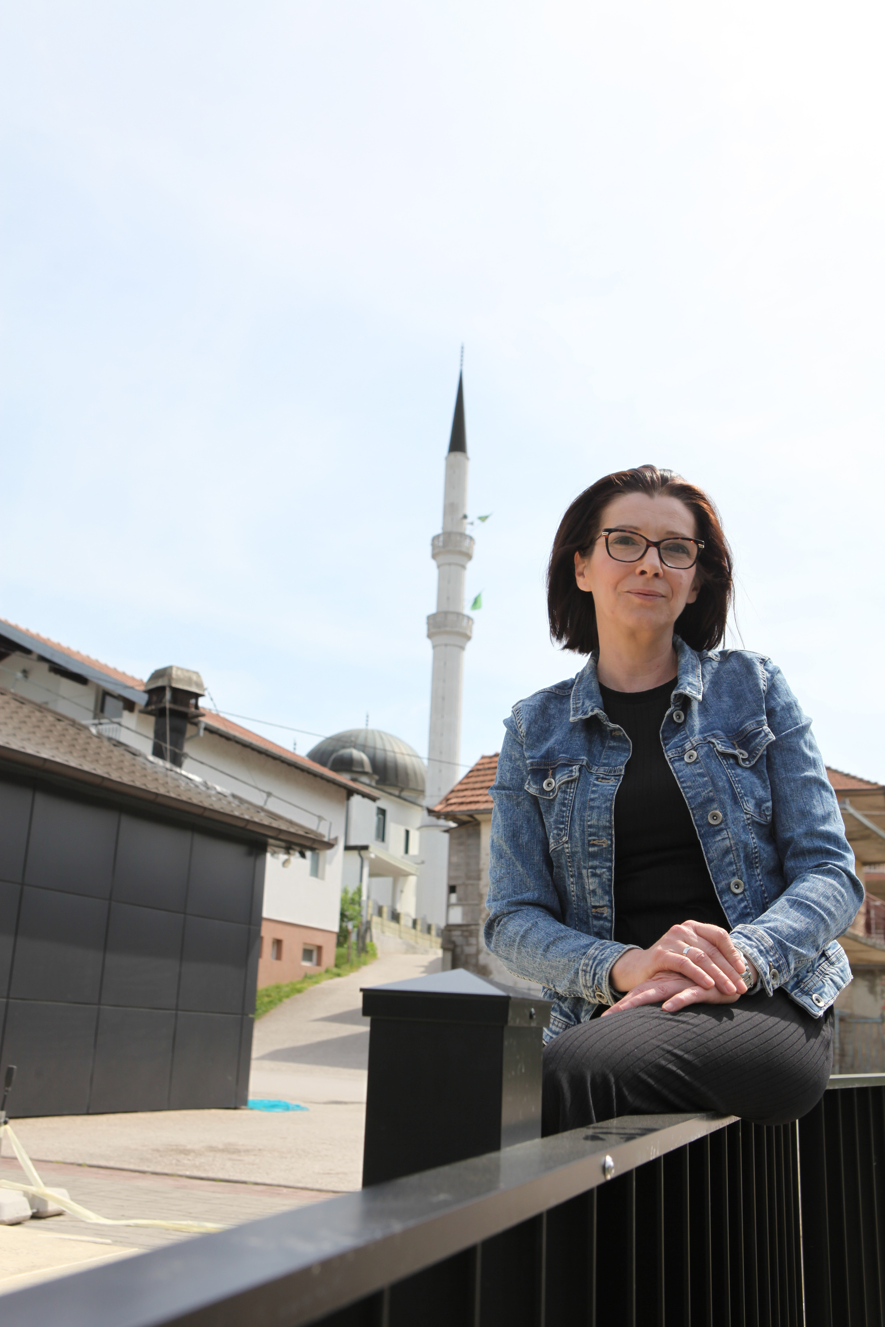 A person with glasses standing in front of a mosque