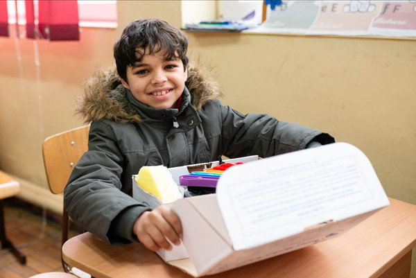 a child smiling whilst he opens a shoebox full of donated supplies
