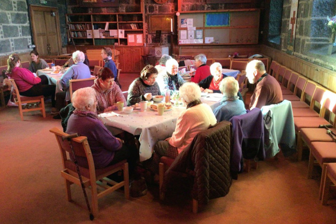 a group of elderly people sat at a table eating and drinking