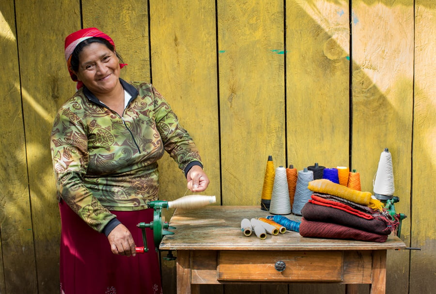 A woman stands proudly in front of sewing equipment and fabric