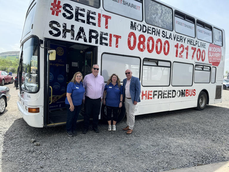 a group of people standing in front of a double decker bus raising awareness of modern slavery