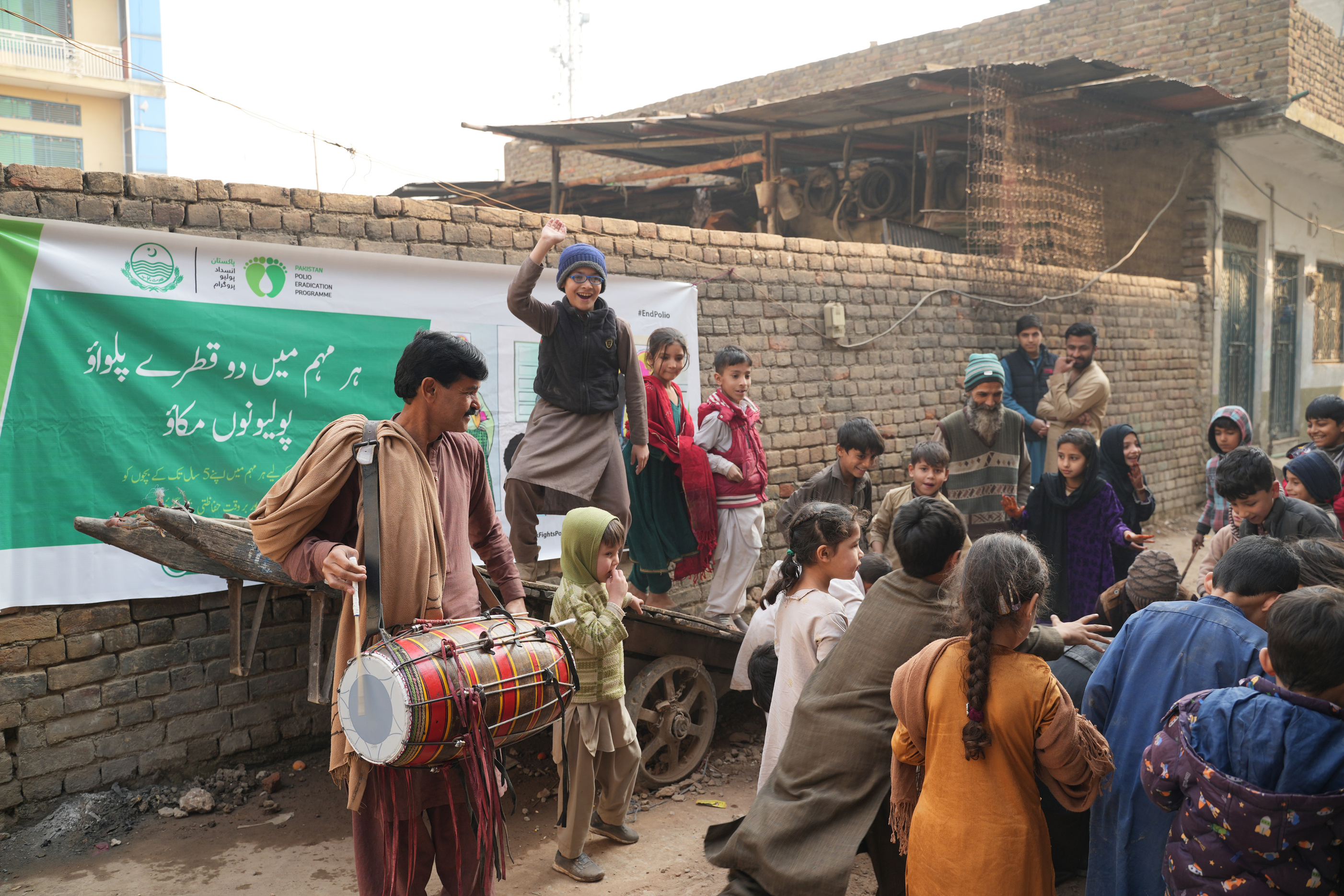 a group of children playing in the street with a person holding a drum