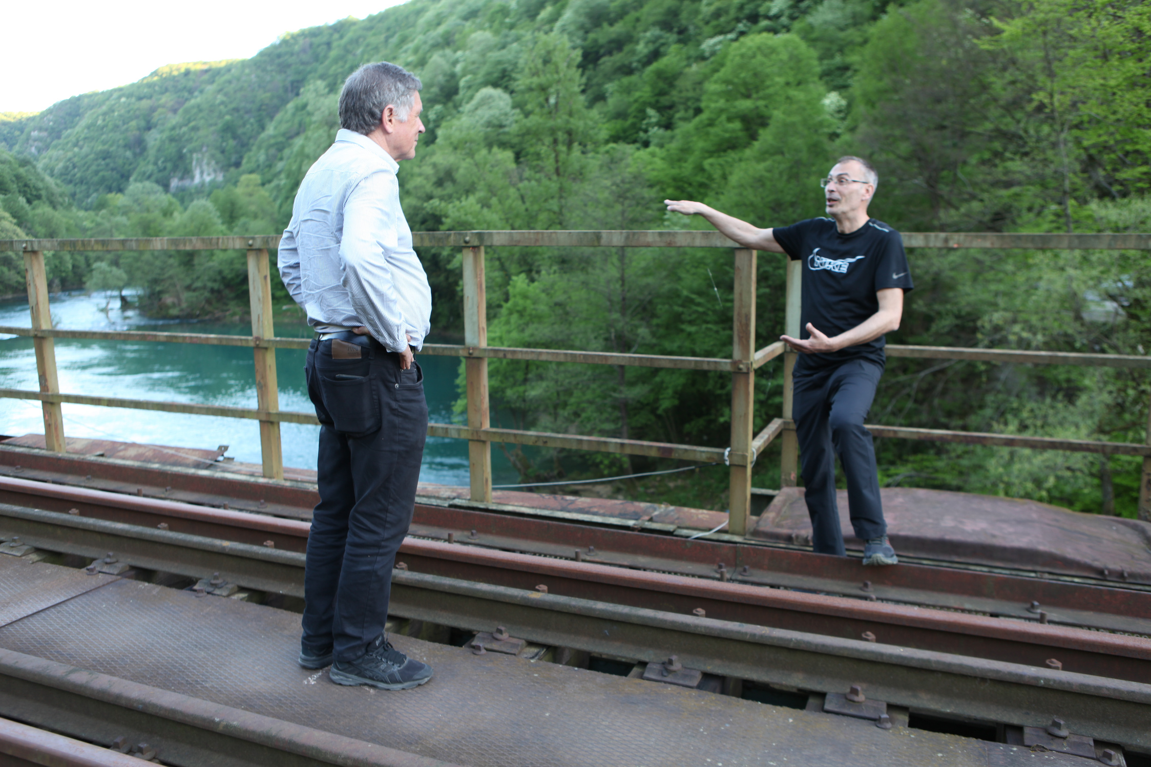 two people standing on a train track near a river