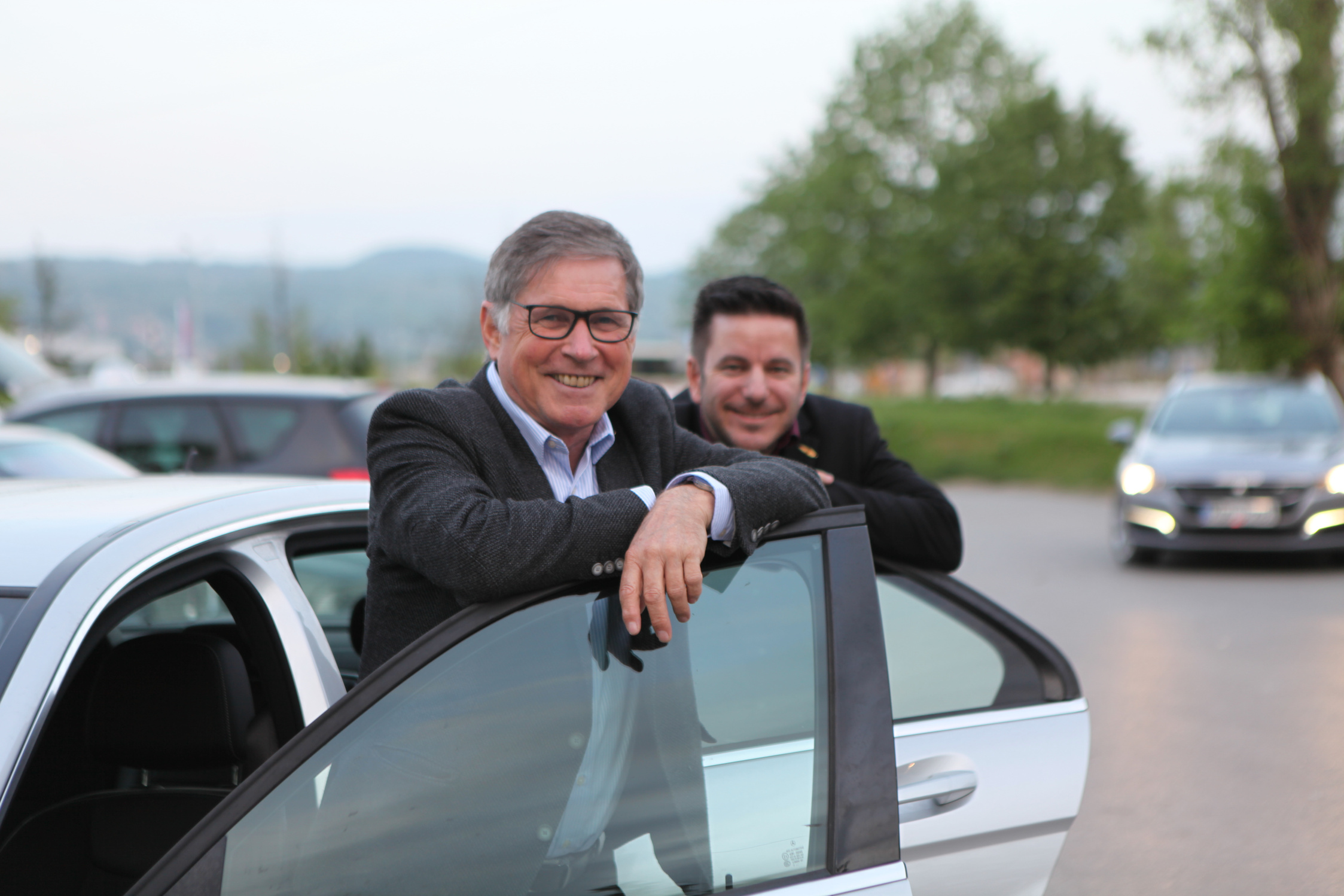 two individuals in suits leaning on the open door of a car