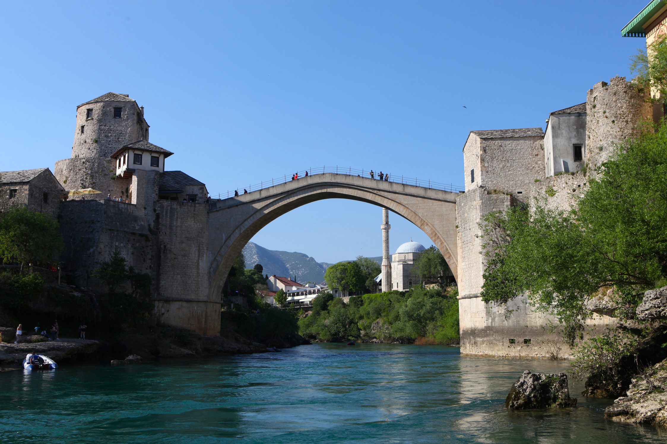 A stone bridge over a river in Bosnia, surrounded by stone houses and buildings