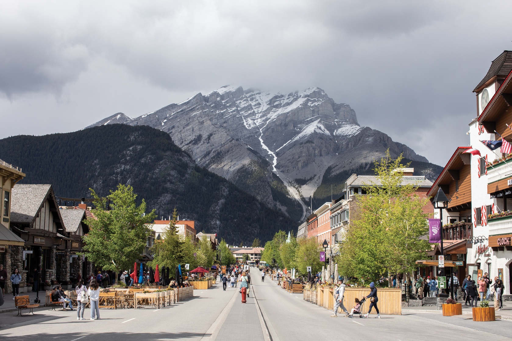 people walk down the middle of a street with mountains in the background - Banff