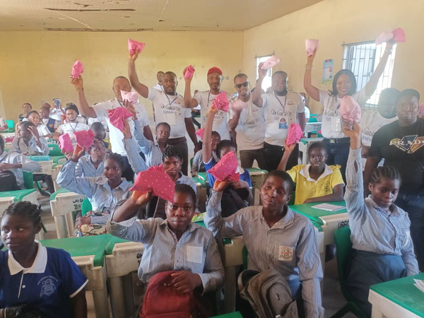 A group of people in a classroom holding pink bags in the air.
