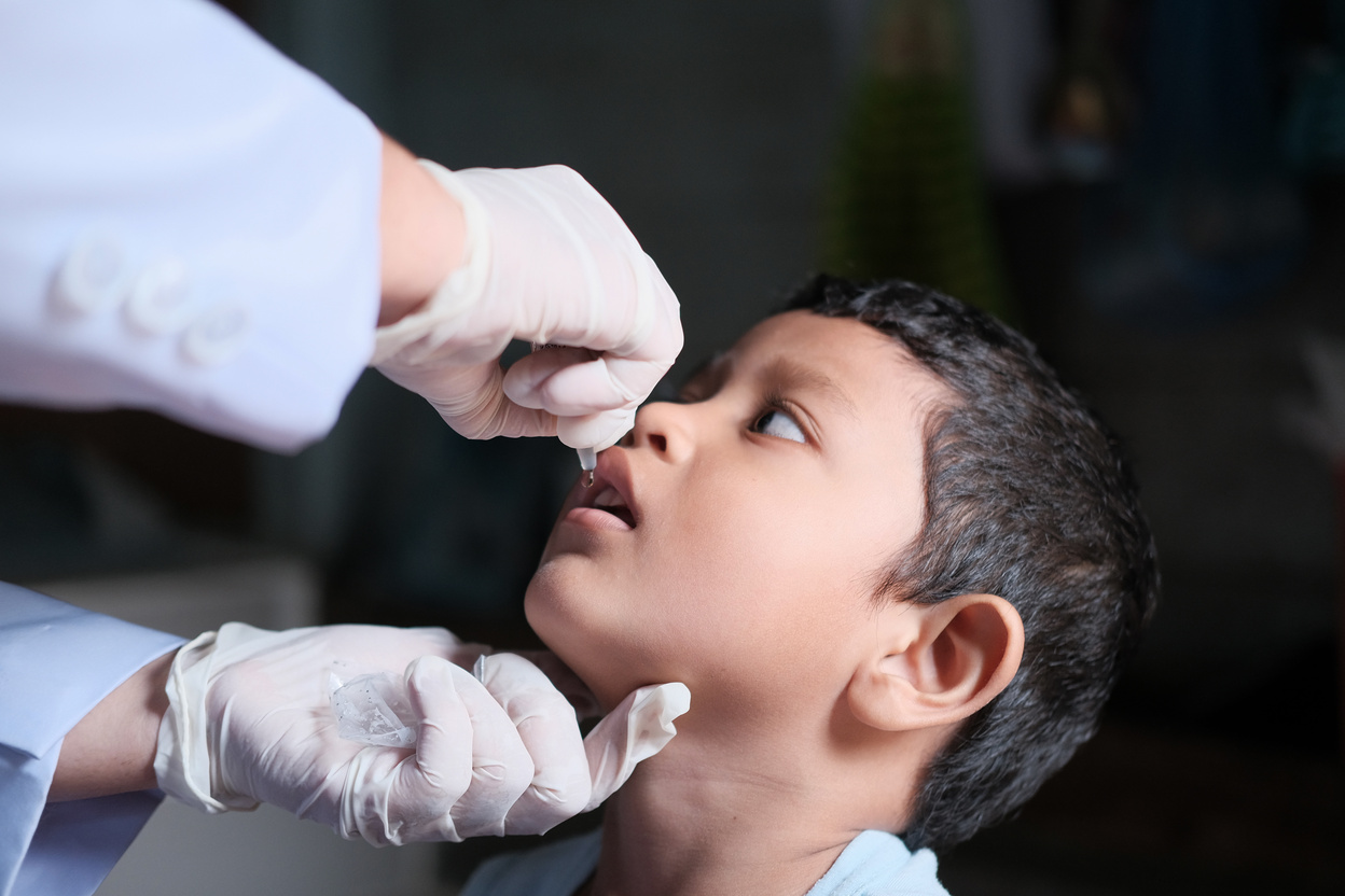 A young person receiving an oral vaccine from a doctor.