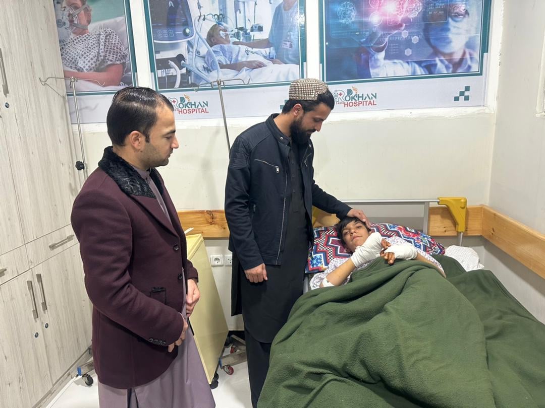 Two men standing next to a boy in a hospital bed with bandages on his hands.