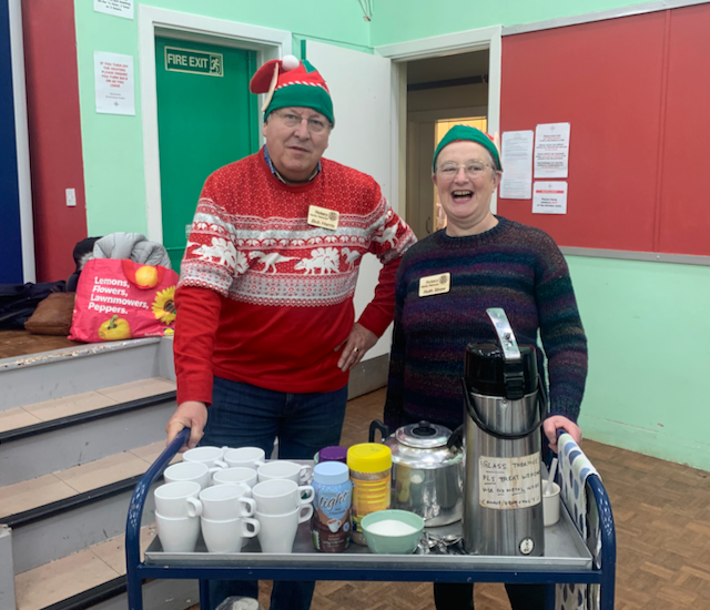 A person and another person in Christmas sweaters standing in front of a table