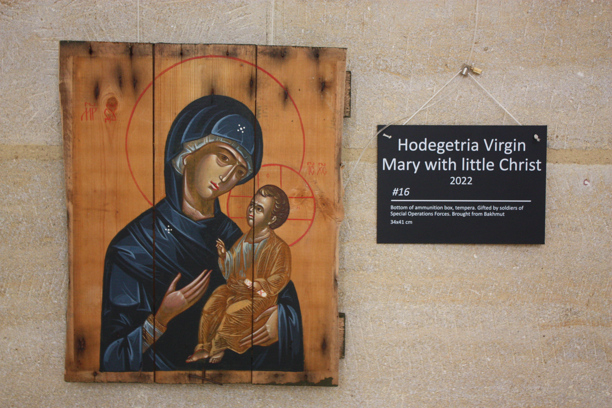 A painting of the Virgin Mary holding a baby Jesus is painted decoratively on a scorched wooden board.