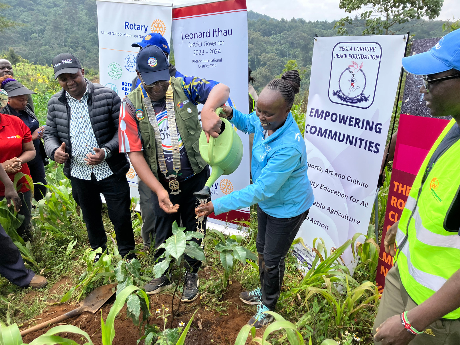 Two people in Kenya in front of Rotary banners watering plants