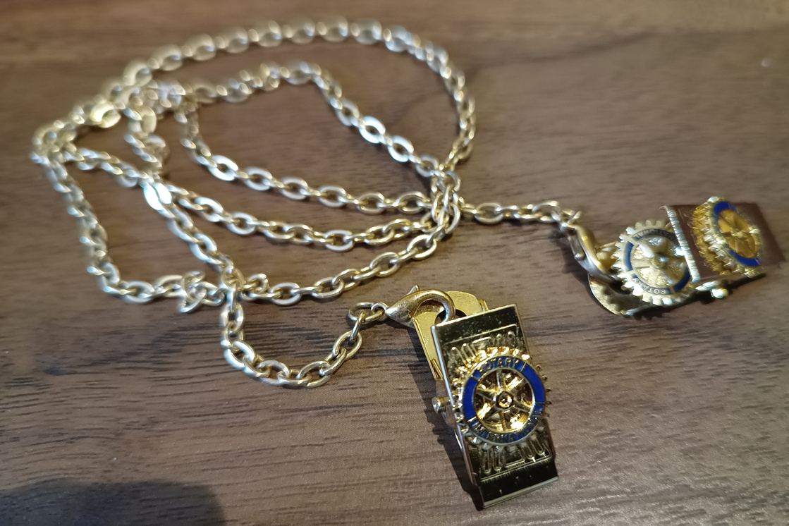 a gold necklace with a blue and white Rotary pendant on it