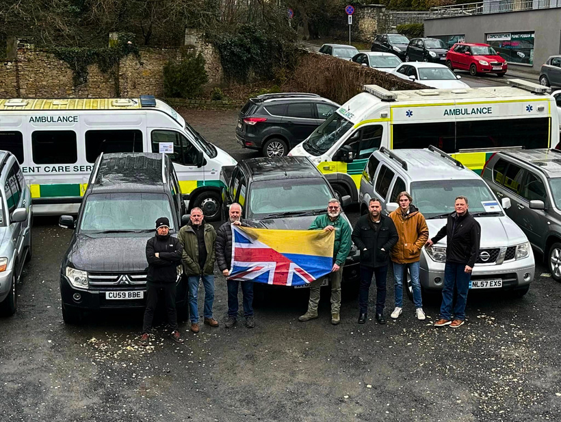 A group of people standing in front of ambulances with a half British, half Ukrainian flag.