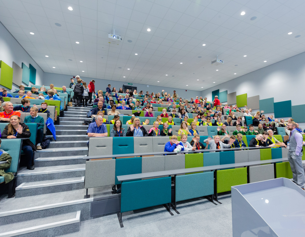 A large lecture hall with many people in it waving at the camera.