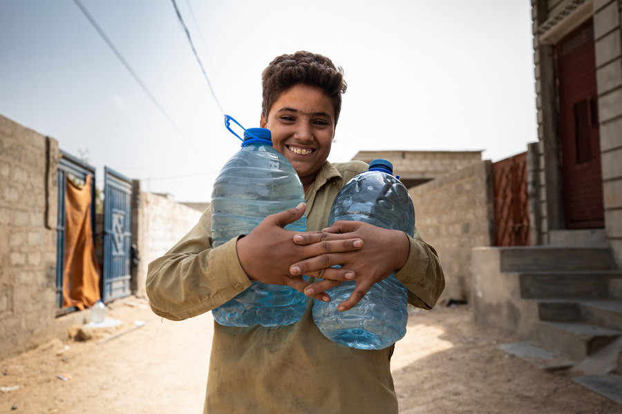 A smiling young boy holds two large bottles of clean water