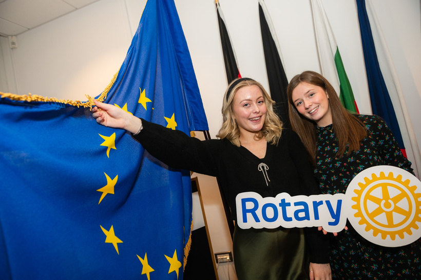 two young women next to EU flag holding Rotary logo banner