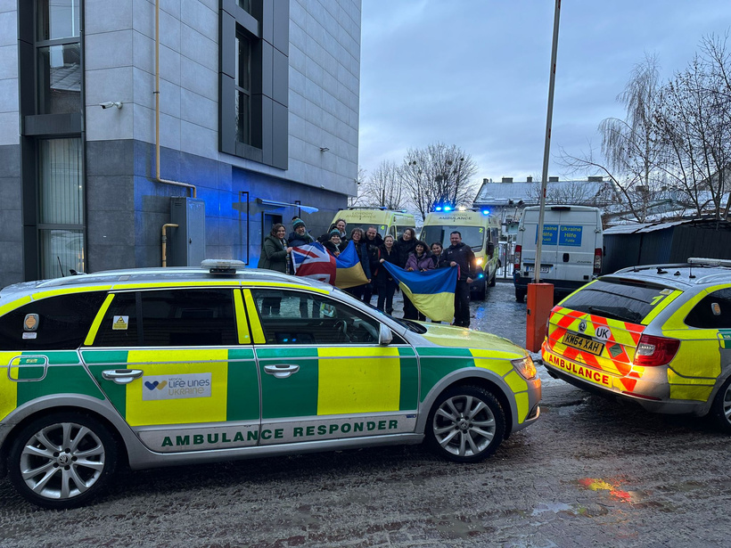 two ambulances parked in front of people holding UK and Ukrainian flags