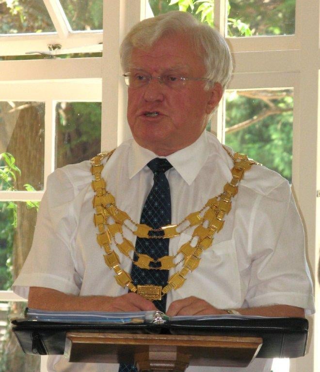 John in a white shirt and wearing his Rotary chain standing at a podium.