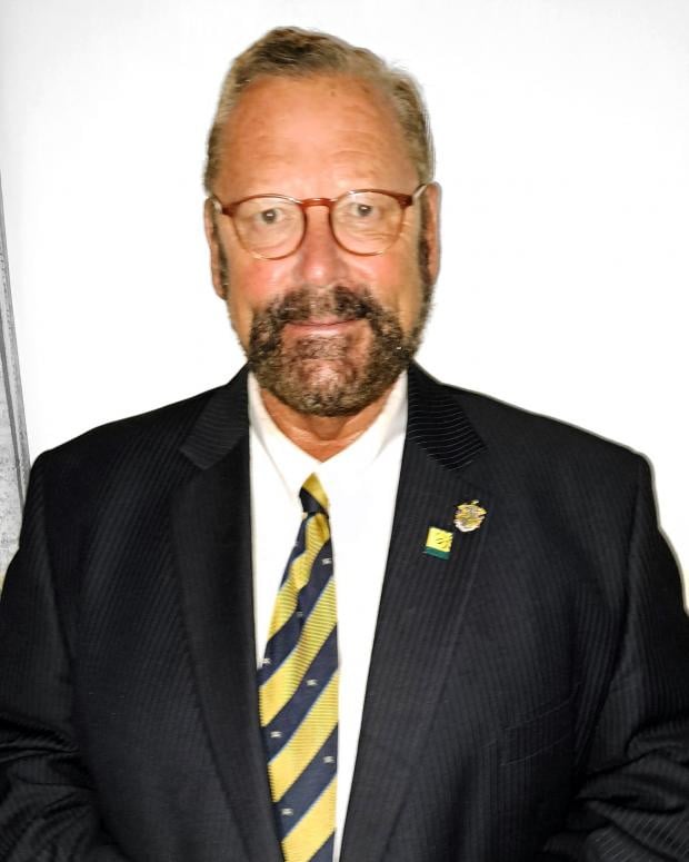 The Reverend Chris Colledge in a suit and tie standing in front of a white wall.