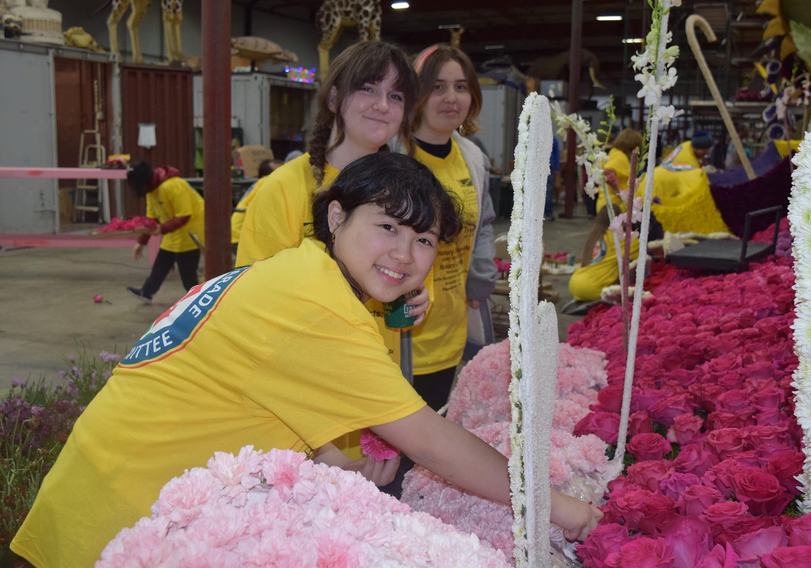 A group of people in yellow shirts are decorating a festival float with flowers.