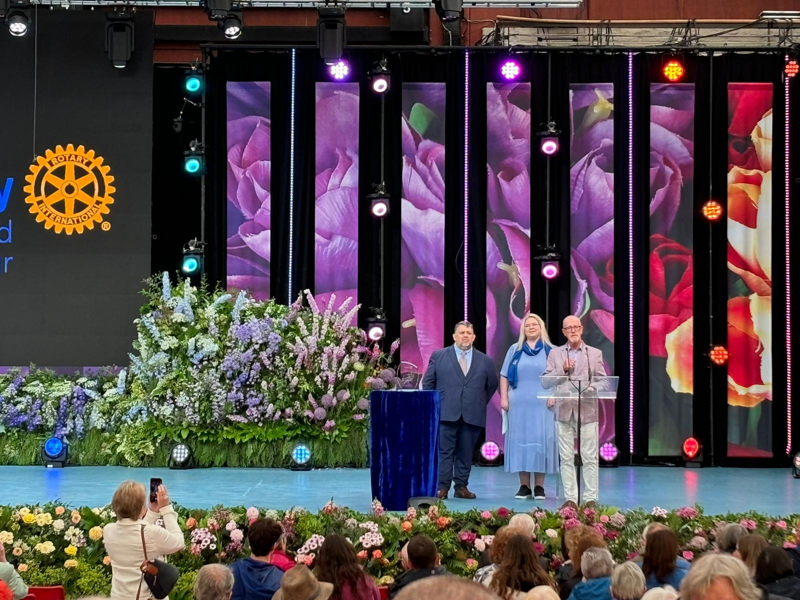 a group of people on stage with flowers in the background