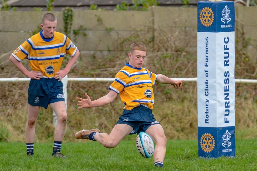 a person in a yellow and blue jersey is kicking a rugby ball with Rotary logos on the advertising boards behind the pitch