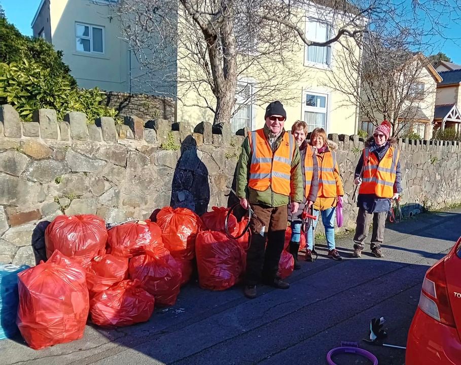 a group of people in orange vests standing next to bags of rubbish