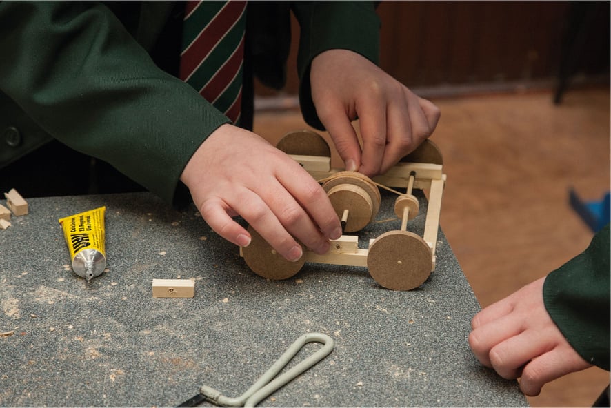 Two people working on a wooden invention on a worktable.