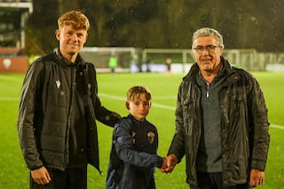 Two individuals shaking hands with a young child on a football field.