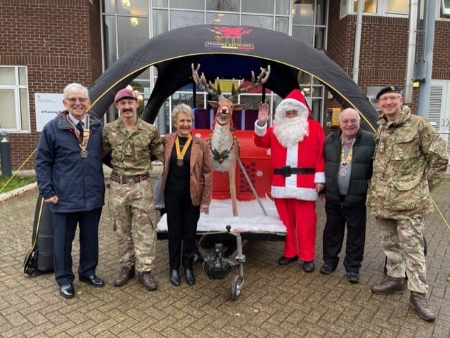 A group of people, including two army officers, posing with Santa Claus and a raindeer.