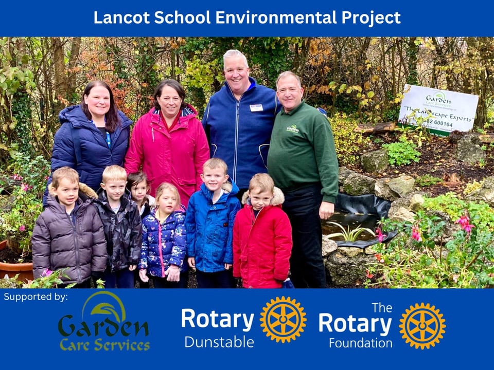 A group of adults and children in coats standing in front of trees and a pond.