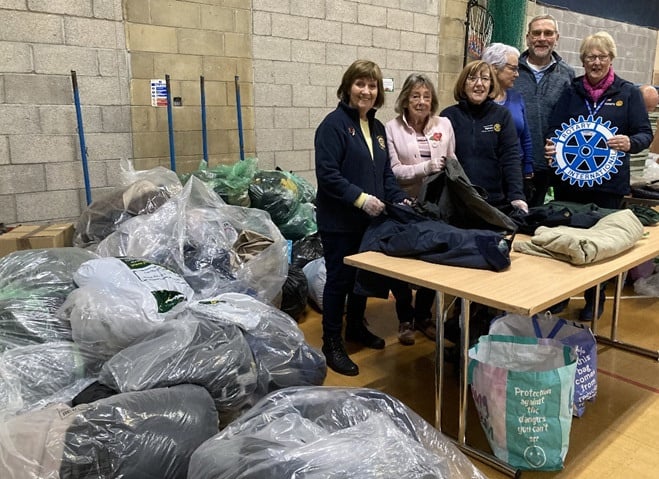 a group of Rotary volunteers standing around a table with bags of donated clothing