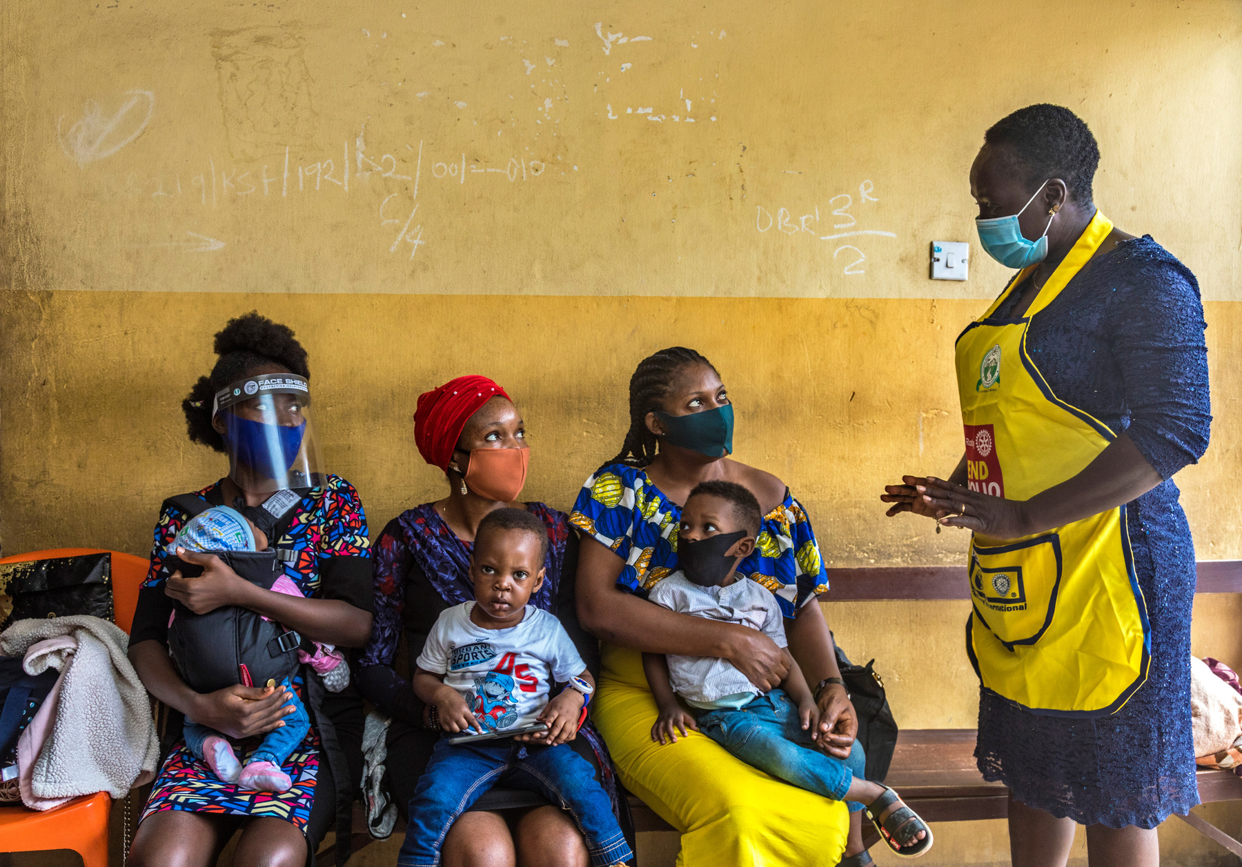 a Rotary volunteer speaking to a group of mothers holding their babies and wearing facemasks