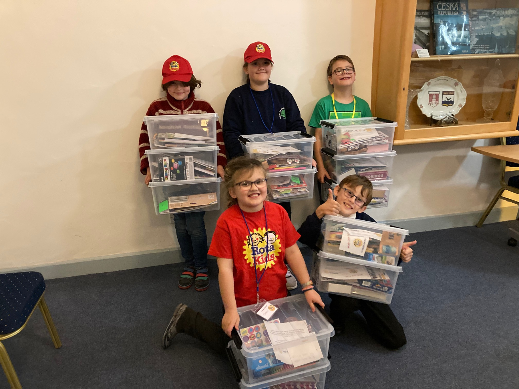 a group of children in red hats and glasses holding boxes of books