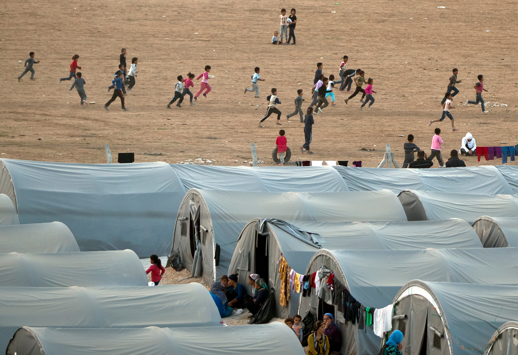 A group of people running around a refugee camp in the desert in Turkey.