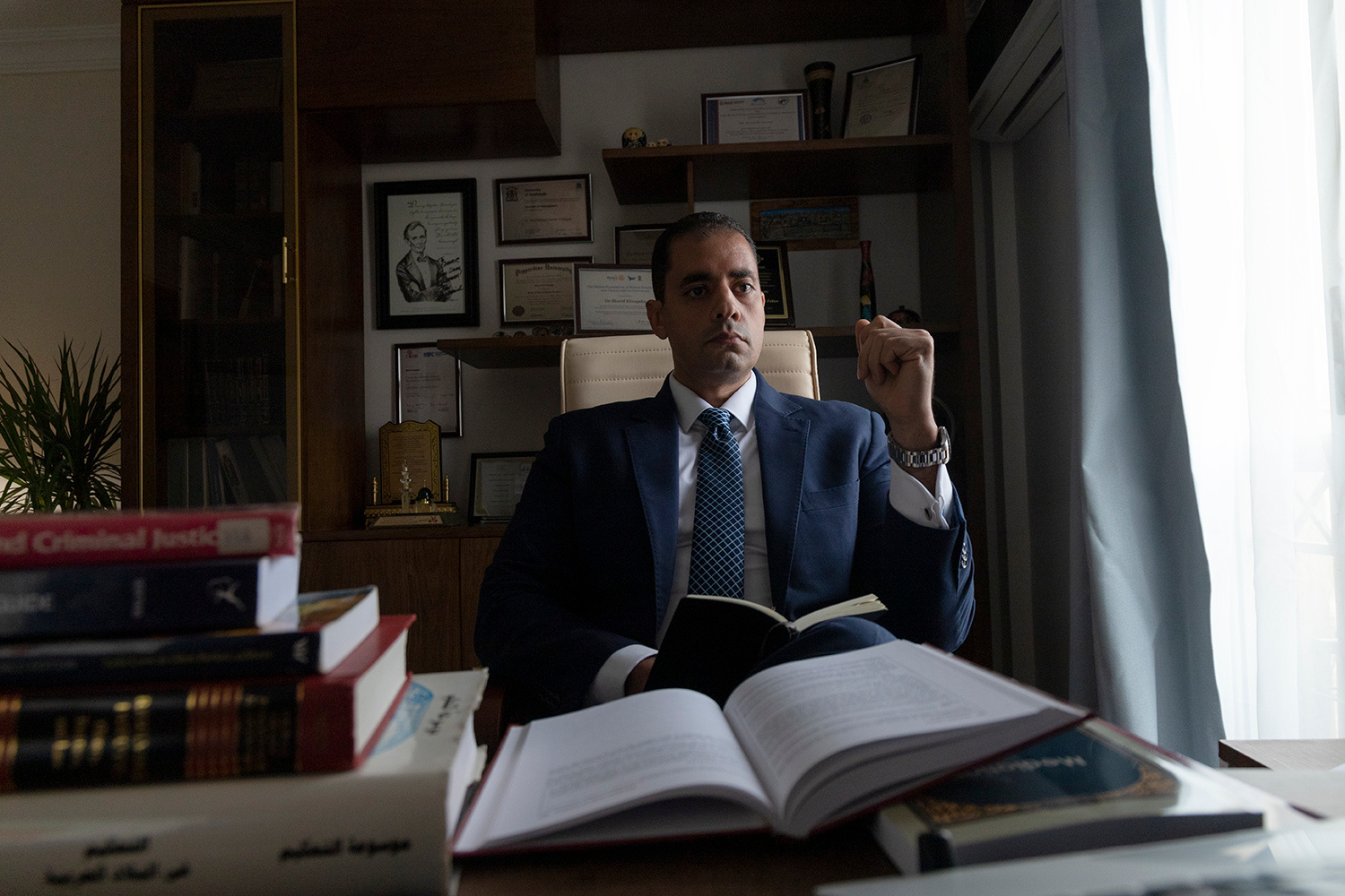 Sherif Elhegahy in a suit sitting at a desk with books.