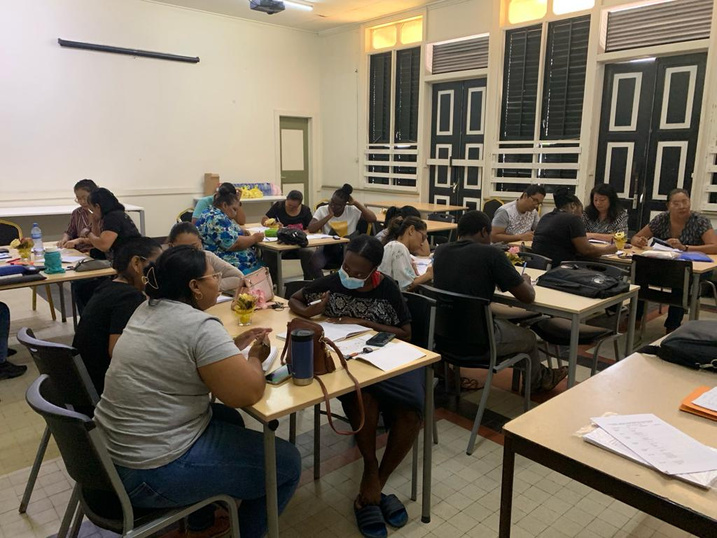 a group of people sitting at tables in a classroom writing