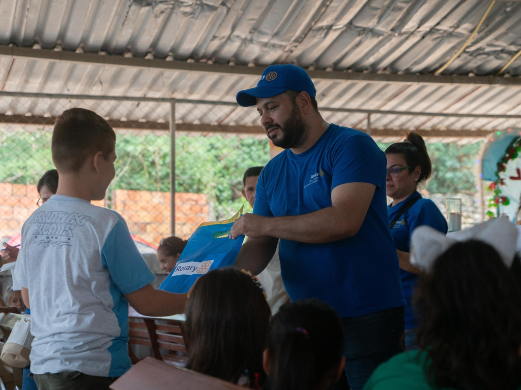 a person in a blue Rotary shirt handing a package to a young person