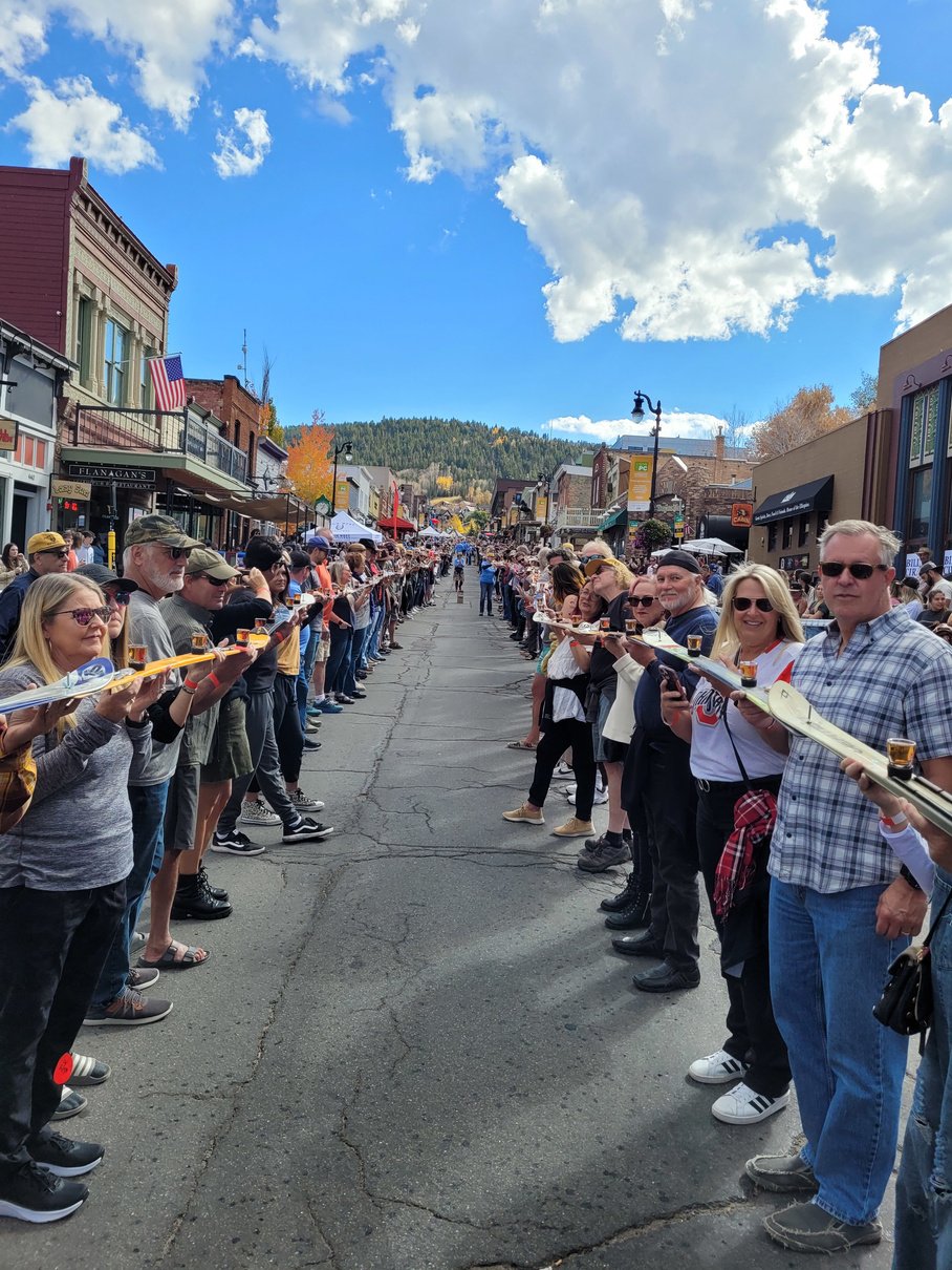 A long line of people standing in the road whilst holding skis balancing shot glasses.