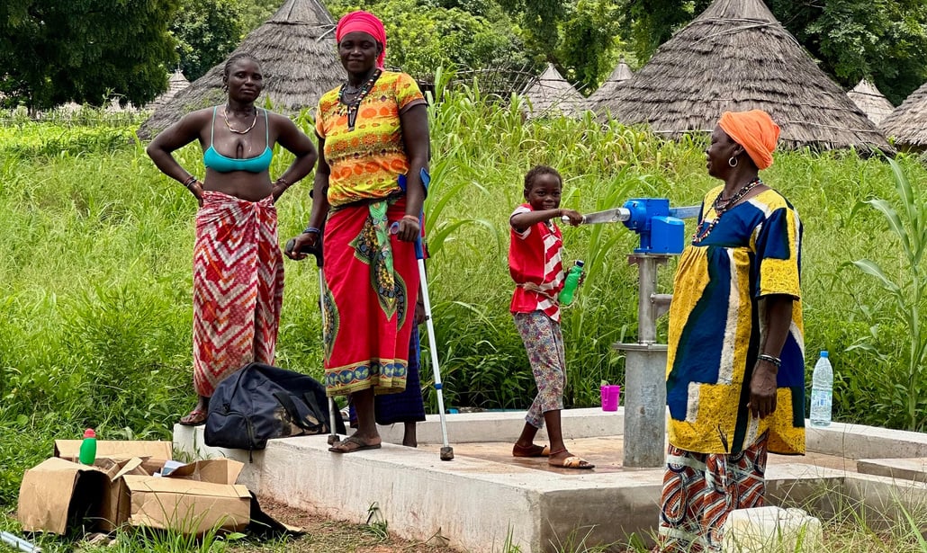 Two women and a child standing around a water pump.