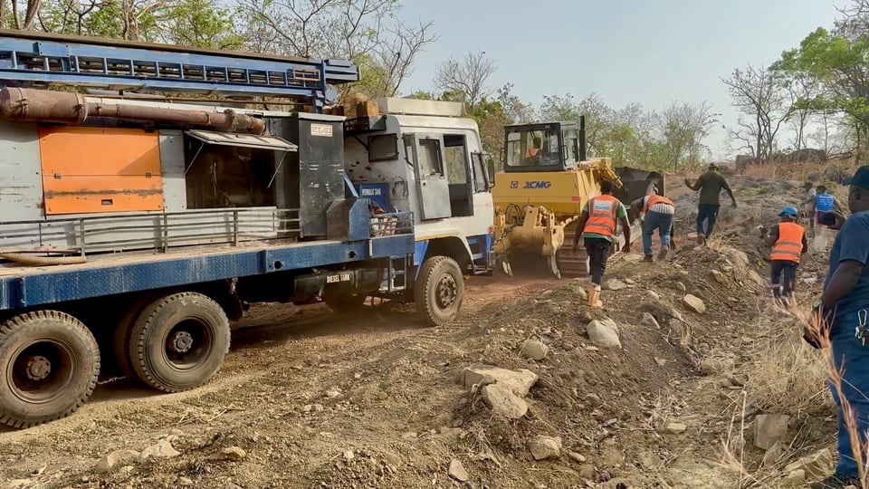 A group of construction workers standing next to a truck on the side of a dirt road.