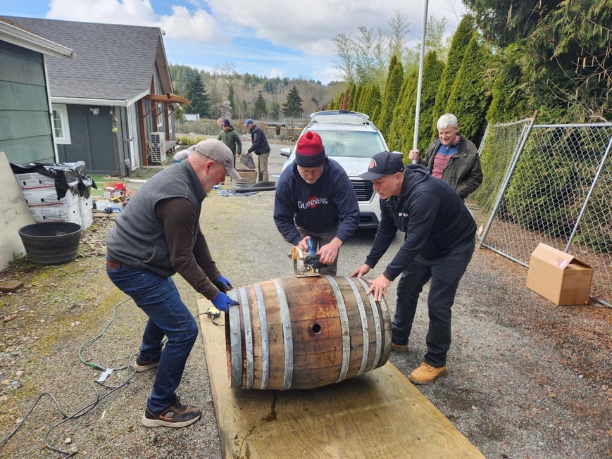 three men are working on a barrel in front of a house