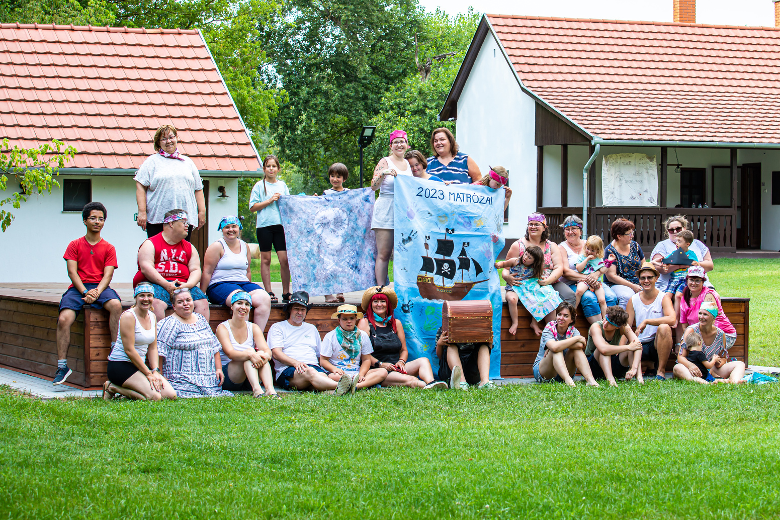 a group of volunteers and children at a summer camp posing for a picture in front of a house