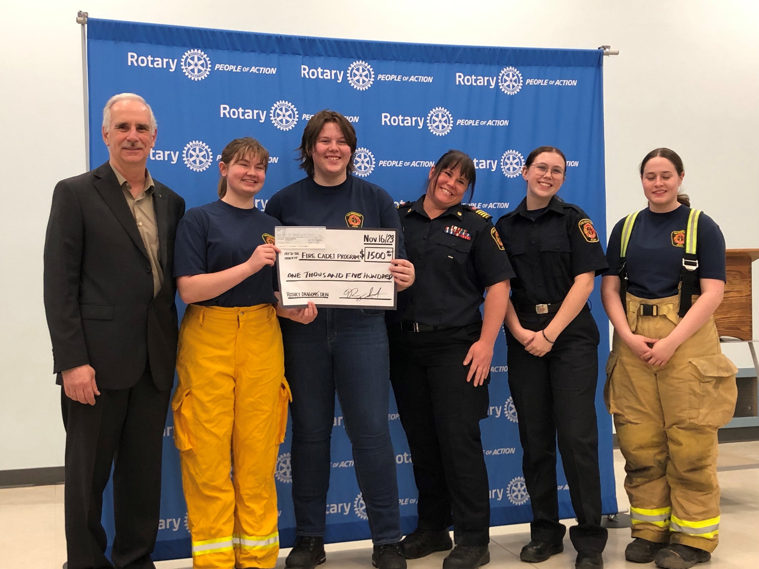 a group of fire department cadets standing in front of a blue wall receiving a cheque