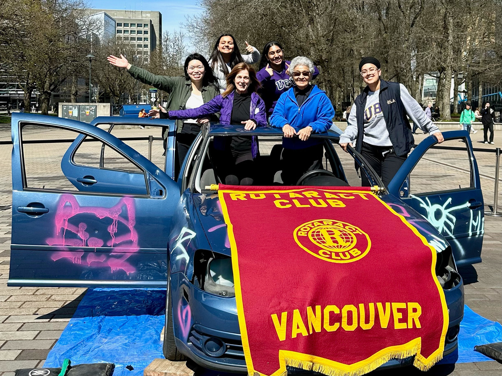 a group of people posing in front of a car with a banner that says Rotaract vancouver