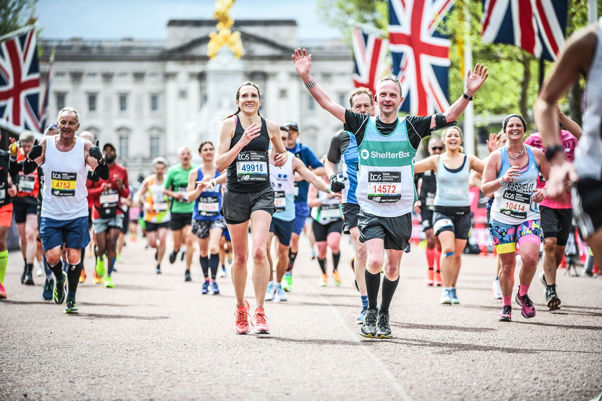 marathon runners complete the race down The Mall in London. One runner is wearing a ShelterBox top.